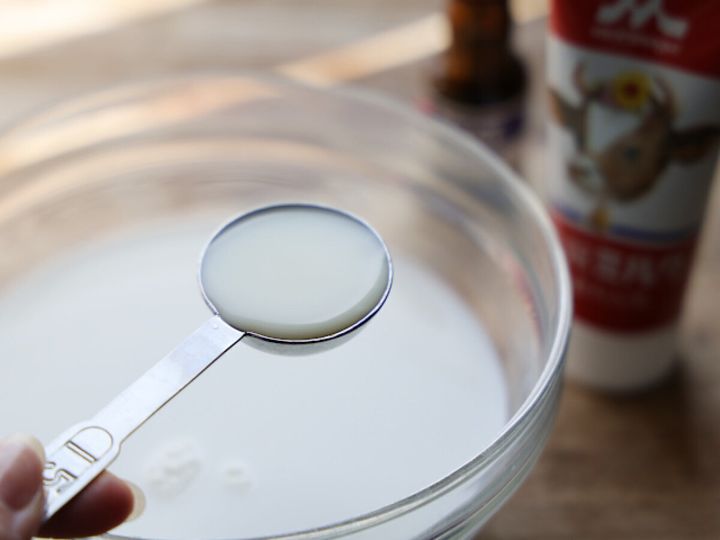 ガラスの大きなボウルに注いだ牛乳の上で、計量スプーンに練乳をすくって持ち上げているところの写真。背景に牛乳パック