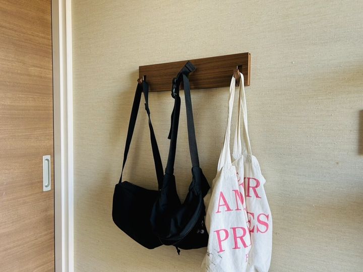 玄関の壁掛けフックに黒いボディバッグと白いトートバッグを掛けて定位置収納している様子