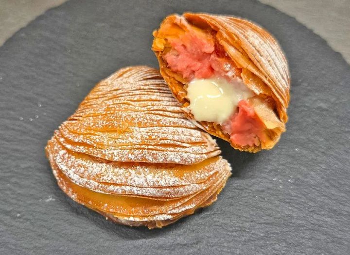 層状のパイ生地を半分に割ったスイーツの断面。内側にピンク色のクリームと白いクリームが詰まった構造が確認できる