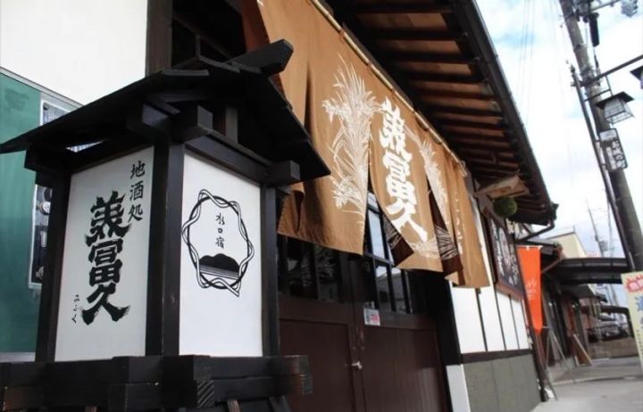 地酒処「兼冨久」の店舗外観。木製行灯看板と水口宿の印、茶色の大型暖簾が軒に下がる老舗酒販店の正面ショット