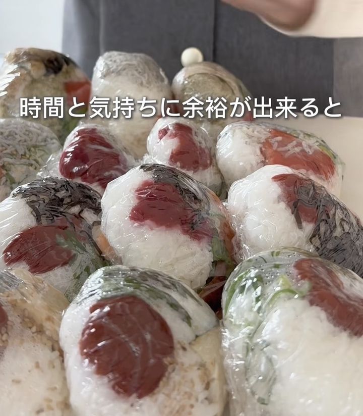Pile of plastic-wrapped onigiri (Japanese rice balls) with red fillings, ready to eat. Text overlay reads Japanese phrase about having time and space.