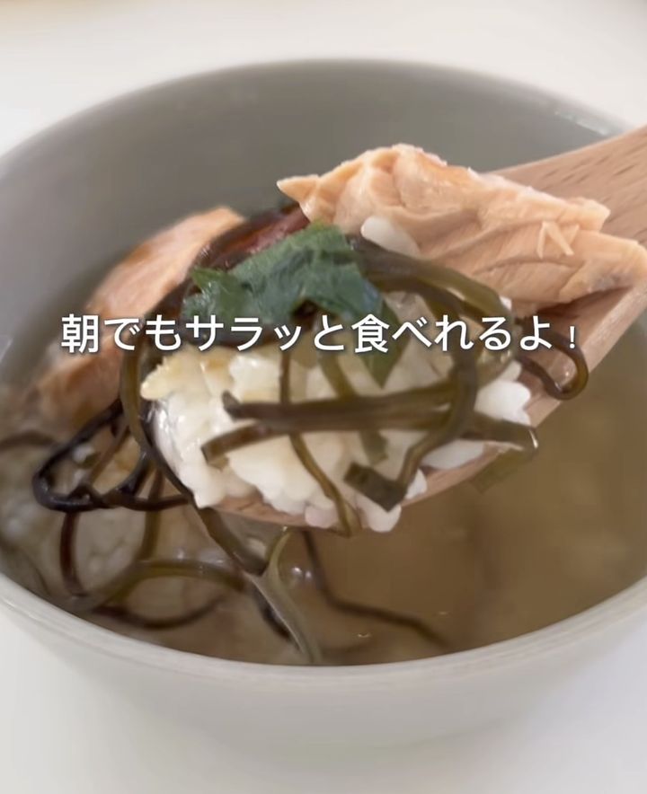 Bowl of clear broth with salmon, tofu, and wakame seaweed, held on a wooden spoon; a light, breakfast-friendly dish.