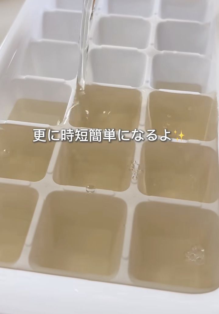 Close-up of a white ice cube tray with pale amber liquid filling several compartments, a stream pouring into the tray.