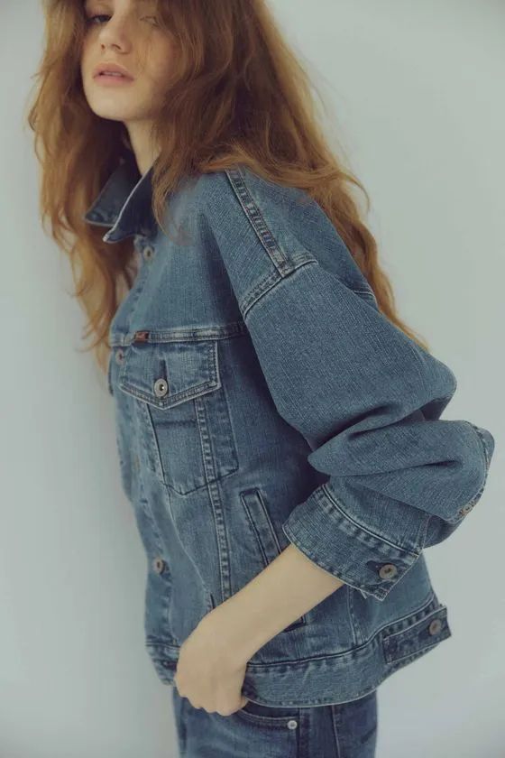 YANUKブランドのデニムジャケットを着た女性モデルの上半身横向きクローズアップ。インディゴブルーのデニム素材・ボタン・ポケット仕様が詳細に確認できる
