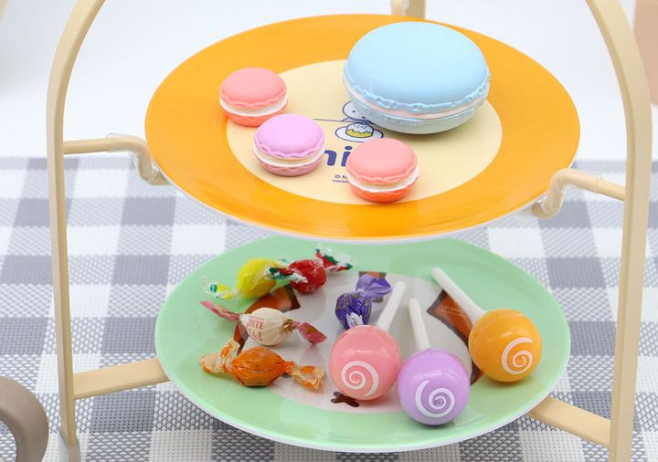 ケーキスタンド上段のオレンジ皿に水色マカロンとピンク・紫のミニマカロン、下段の緑皿にロリポップキャンディと包装紙入りキャンディを盛り付けた写真