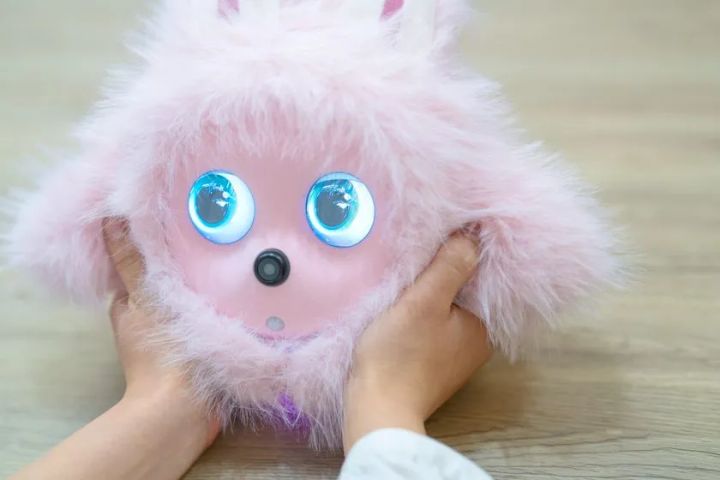 KOTTIピンクモデルを子どもの両手で持つクローズアップショット。青く光るLEDアイとカメラ内蔵ノーズの構造が正面から確認できる