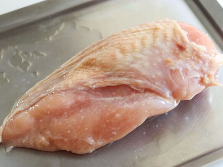 ステンレスバットに置いた皮つき鶏むね肉1枚に塩と酒をもみ込んだ工程写真