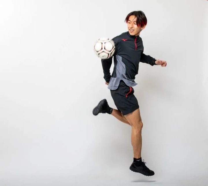 岡部将和氏が同じミズノ製黒ジャージでサッカーボールをインサイドでコントロールしながら空中に浮く全身スタジオ撮影ショット。画像1より左寄り構図で全身バランスと技術動作が見やすい角度