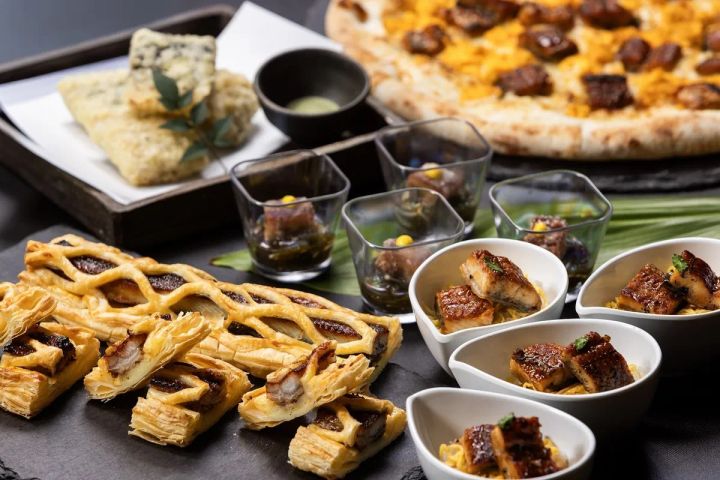 うなぎフェアの複数料理を一堂に並べた集合カット。うなぎ蒲焼き入りパイ生地、小鉢盛りの蒲焼き、ガラスカップ入りうなぎゼリー寄せ、うなぎピッツァ、天ぷらが石板上に配置されている