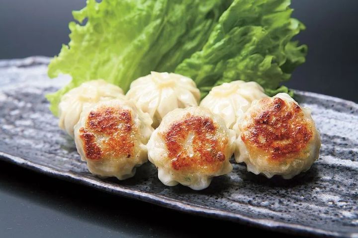石板皿に盛られた焼きシュウマイ4個のアップショット。上面に焼き色がついており、レタスを添えた博多グルメの商品写真