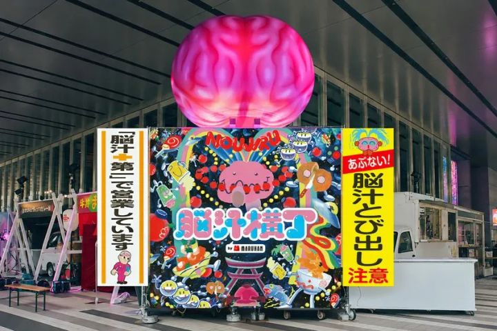 脳汁横丁 by MARUHANのイベント入口外観。上部に巨大なピンク色の脳オブジェを配し、カラフルなポップアートの看板と「脳汁とびだし注意」の縦幕が設置されたベルサール秋葉原会場前の実写撮影カット