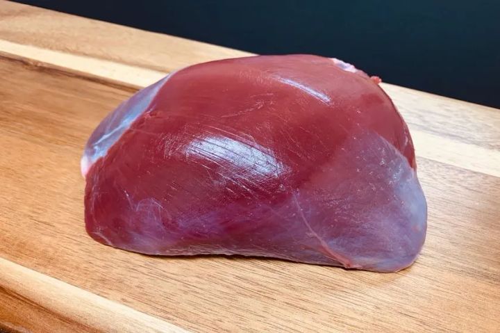木製まな板の上に置かれた皮付きジビエ肉の塊。薄い膜（シルバースキン）に覆われた濃い赤色の大きなブロック肉で、シカのモモ肉または肩ロースと見られる