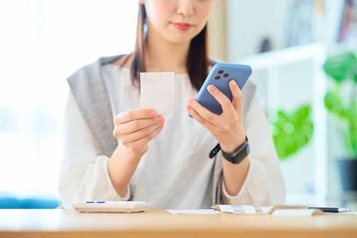 レシートとスマートフォンを手にした若い女性