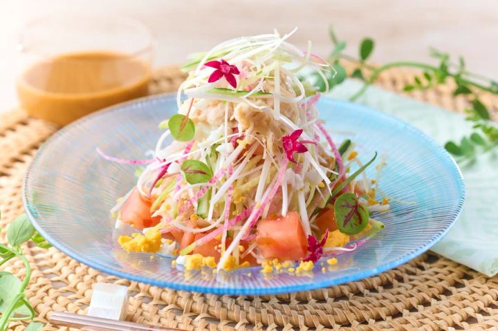 青いガラス皿に盛ったカニほぐし身とトマト・大根千切り・食用花のサラダの単品クローズアップ写真