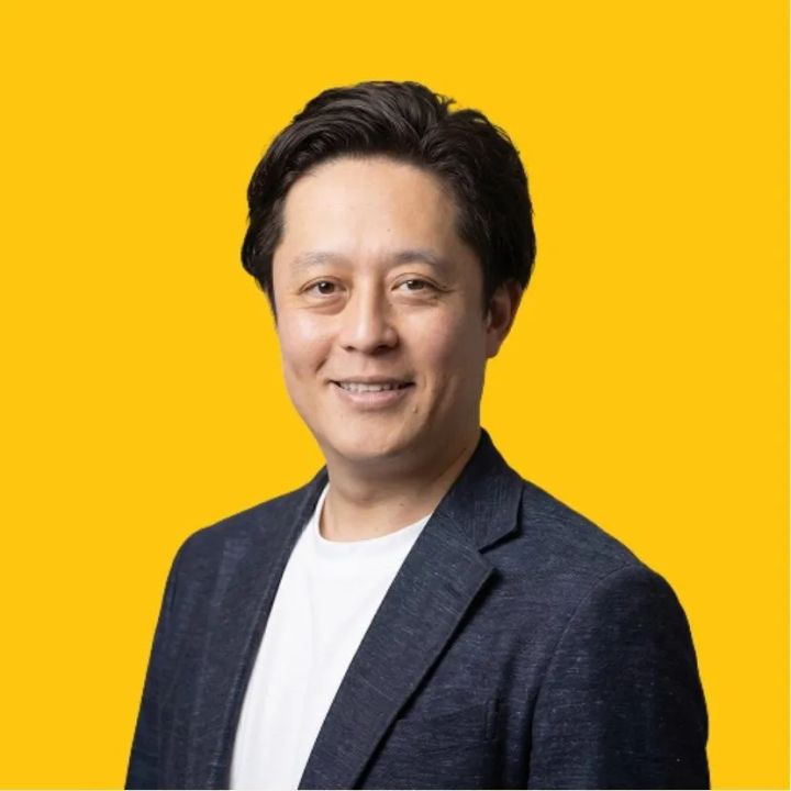 ユームテクノロジージャパン代表取締役・松田しゅう平氏の公式プロフィール写真。黄色背景にネイビージャケット着用の上半身ショット