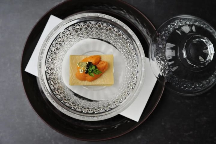 クリスタル皿に盛られたウニとキャビアの前菜料理。薄いクレープ状の台座に橙色のウニを乗せ、金箔とキャビアをあしらい、パセリを添えた一品