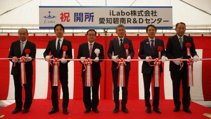 iLabo株式会社 愛知碧南R&Dセンターの開所式典でスーツ姿の関係者6名がテープカットを行っている集合写真、祝開所の横断幕を背景に撮影