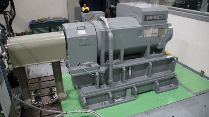 愛知碧南R&DセンターのMEIDEN製大型発電機・試験装置を室内で撮影した写真。グレー色の本体とマウント台座、配線類が確認でき、水素燃焼エンジン研究用の動力計測設備とみられる