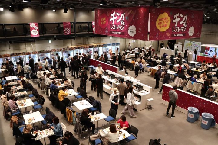 チン！するレストランin SAPPOROの会場全景で、冷凍ショーケース列・電子レンジステーション・多数の来場者が着席して食事する様子を上方から俯瞰した写真