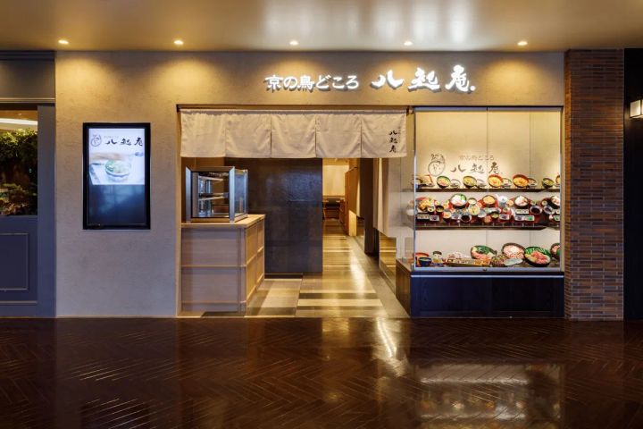 京の鳥どころ八起庵の店舗外観。暖簾と店名看板、右側に鶏・鴨料理の食品サンプルケース、左側にデジタルサイネージが設置された百貨店内レストランの入口全景。