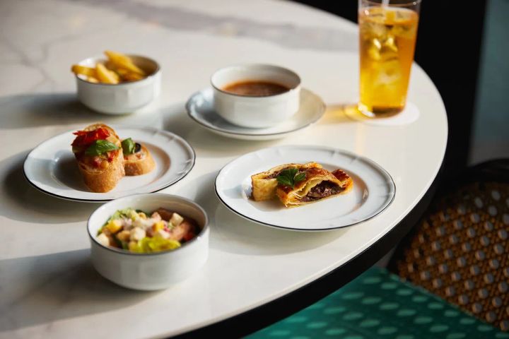 大理石テーブルに並ぶセイボリー5品。トマトブルスケッタ、ビーフパイ、野菜サラダ、フライドポテト入りスープ、アイスティーが自然光の中で整然と配置されている