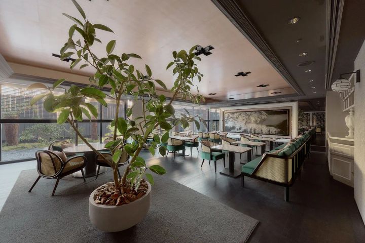 La Jyho Terrace（ラジョ テラス）の店内全景。大型観葉植物2本を前景に、緑色のベルベットチェアとラタン素材のソファが並ぶダイニングエリア、庭園に面した大窓、奥壁面の山水画アートを収める空間構成。