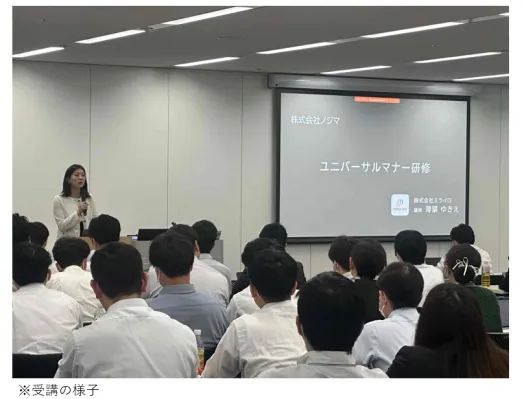 株式会社ノジマのユニバーサルマナー研修の受講風景。会議室で複数の受講者がスクリーン前の女性講師の説明を聞いており、スクリーンに研修タイトルと株式会社ミライロ講師名が映っている