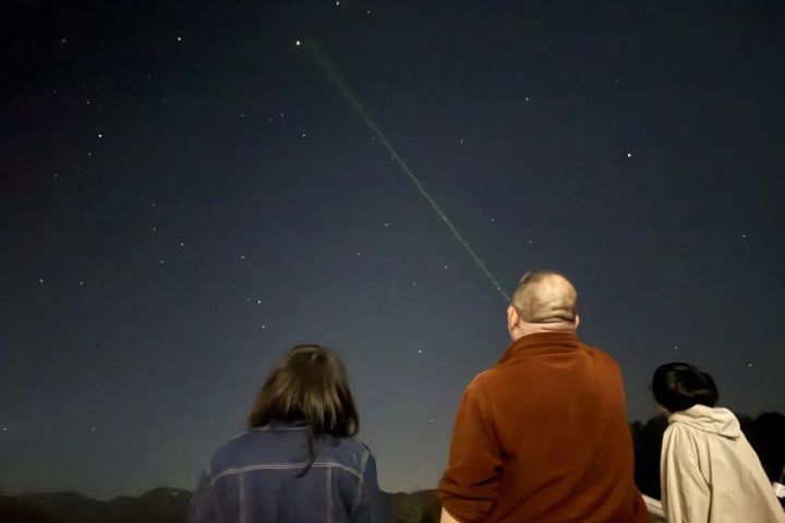 3人の参加者が屋外で夜空を見上げ、グリーンレーザーポインターで星座を指し示す星空観察体験のショット