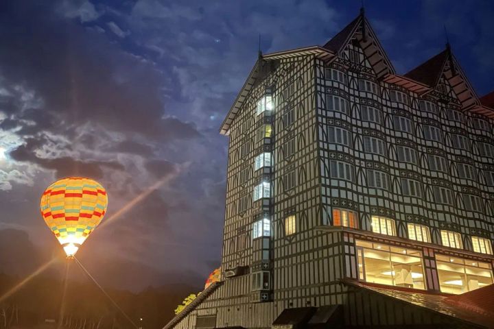 ホテルグリーンプラザ白馬の欧風外観と、夜空に浮かぶ熱気球のバーナー点灯シーン。建物はチューダー様式の木組みデザインで、熱気球体験イベントの夜間開催を示す写真