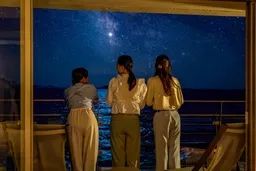 夜間の海を望むバルコニーで3人の女性が星空と天の川を眺めているシーン。海色の夜景と星が広がる屋外展望の宿泊体験を示す