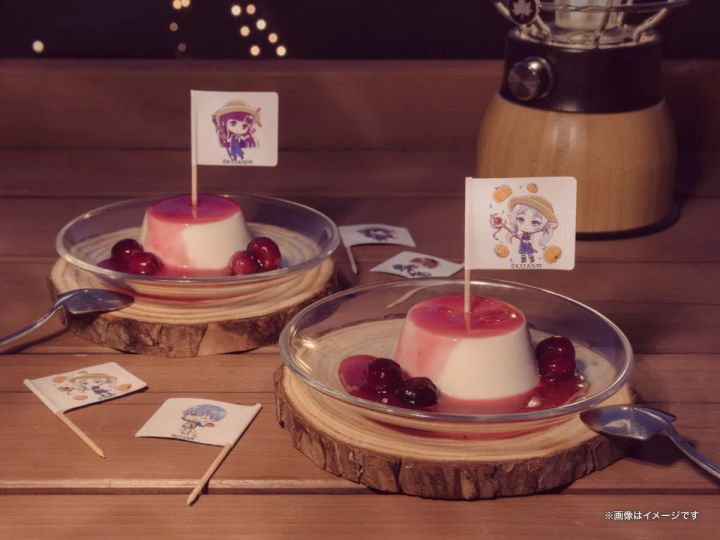 葬送のフリーレンコラボのメルクーアプリン2個を木製コースターに並べた全体ショット。赤いベリーソースとチェリー添え、各プリンにキャラクターデザインの旗刺し、背景にランタンとボケたイルミネーション