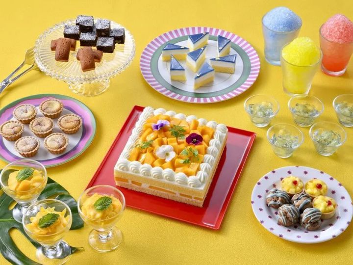 夏のスイーツビュッフェ品揃えを上から撮影した俯瞰写真。マンゴーケーキ・チョコブラウニー・タルト・かき氷ドリンク・パンナコッタなど10種以上のデザートを黄色背景に配置