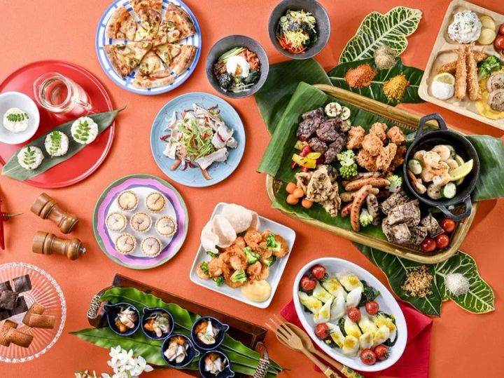 ビュッフェの料理ラインナップを俯瞰撮影した物料写真。グリル肉・唐揚げ・エビ・ピザ・小籠包・カプレーゼ風サラダなどスパイス系HOT料理を中心に約10品以上を並べたテーブルショット
