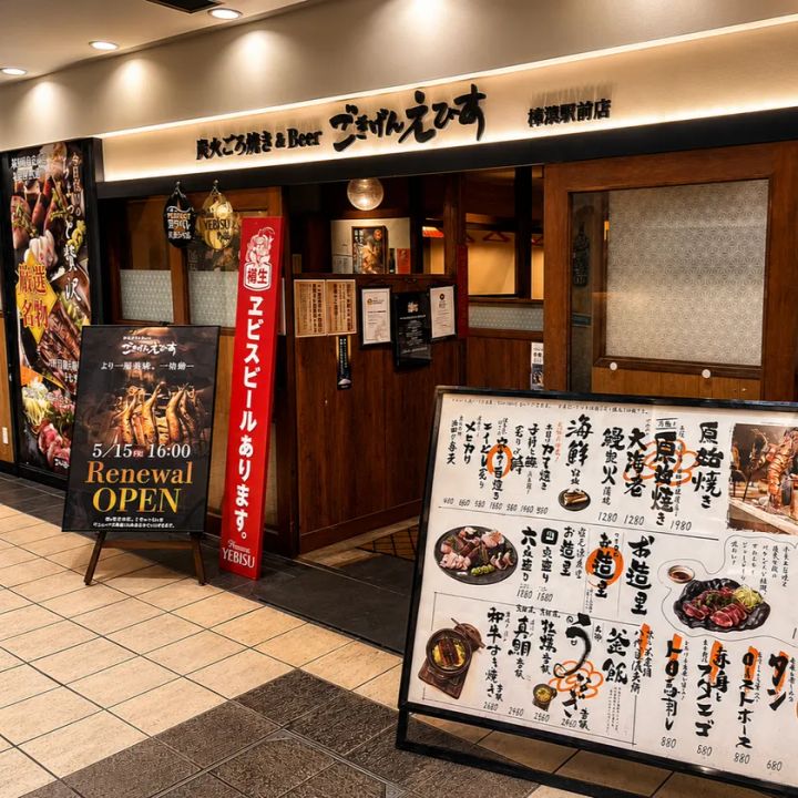 ごきげんえびす樟葉駅前店の外観と店頭看板。5/15 16:00 Renewal OPENの告知幕、ヱビスビール樽生の幟、炭火ごろ焼き＆Beerの屋号看板、メニューボードが写る
