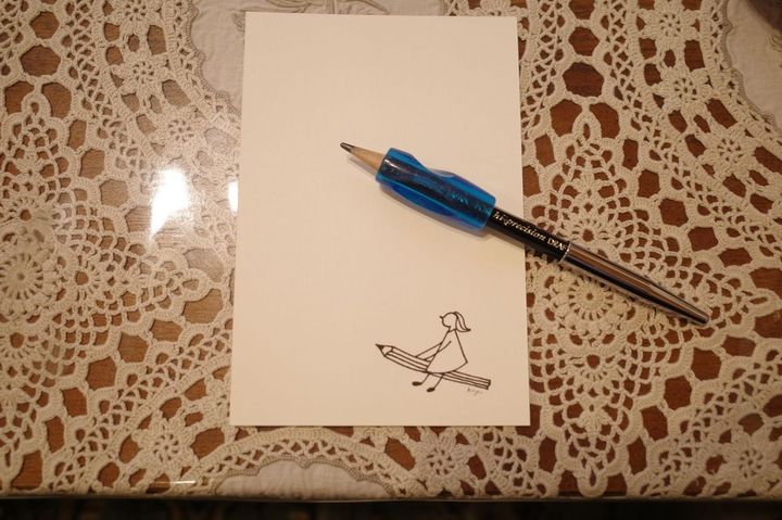 春日さんが愛用するグリップをはめた鉛筆。お孫さんのイラストが入ったはがきとともに