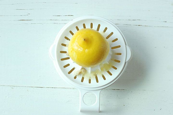 白いプラスチック製のレモン搾り器に皮をそぎ落とし半分にカットしたレモンを乗せ果汁を絞っている俯瞰写真
