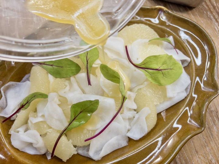 茶色い器に盛ったカブとグレープフルーツに赤軸のベビーリーフを散らしドレッシングをかける完成写真
