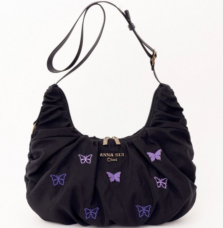 ANNA SUI miniの黒いクロワッサンバッグをショルダーストラップを長く伸ばして斜め掛けできる状態にしたもの。パープルの蝶の刺繍と立体パーツが全面にあしらわれている