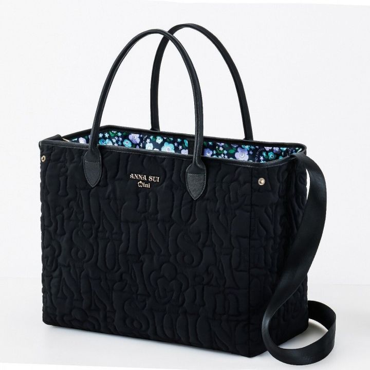 ANNA SUI miniの黒いロゴキルティングのビッグトートバッグ。黒い持ち手とショルダーストラップ、アンティークゴールドのロゴプレートが付き、内側はパープルとブルーの花柄プリント