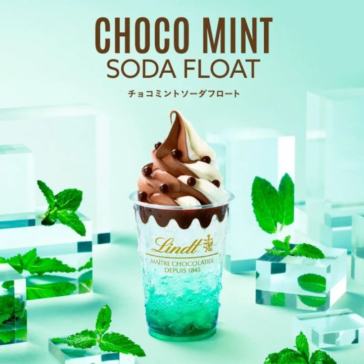 チョコミントソーダフロートの画像。透明なカップに入ったミントソーダの上に、チョコレートとバニラのソフトクリームが乗っています。チョコレートソースとチョコレートボールでトッピングされ、ミントの葉が添えられています。周りには透明なブロックが配置されています。