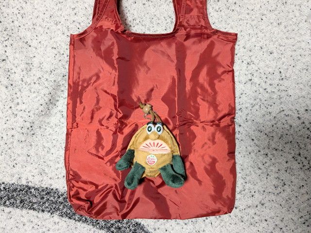 ゼスプリ キウイブラザーズぬいぐるみエコバッグ全体。鮮やかなレッドのエコバッグにキウイブラザーズのぬいぐるみチャームがついている