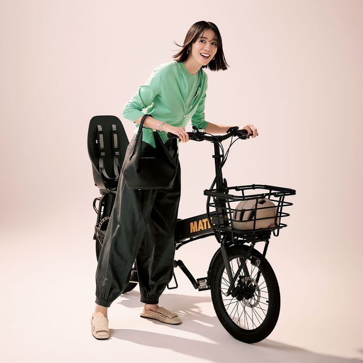 グリーンのニットのセットを着て自転車をひくモデル