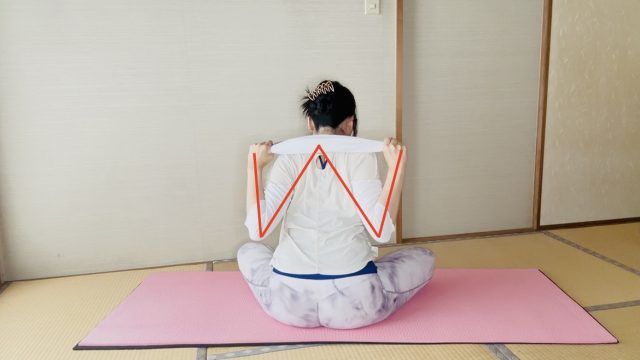 座った姿勢でタオルを肩の後ろに引き、肩甲骨を寄せるエクササイズをする女性