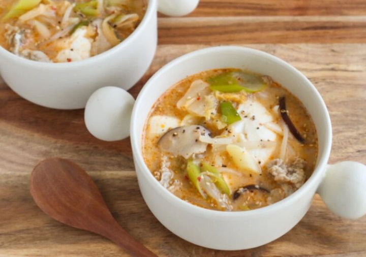 白いスープカップに入った赤みのある豚キムチ豆乳スープ。豆腐・しいたけ・もやし・長ねぎが入り黒こしょうがふられている