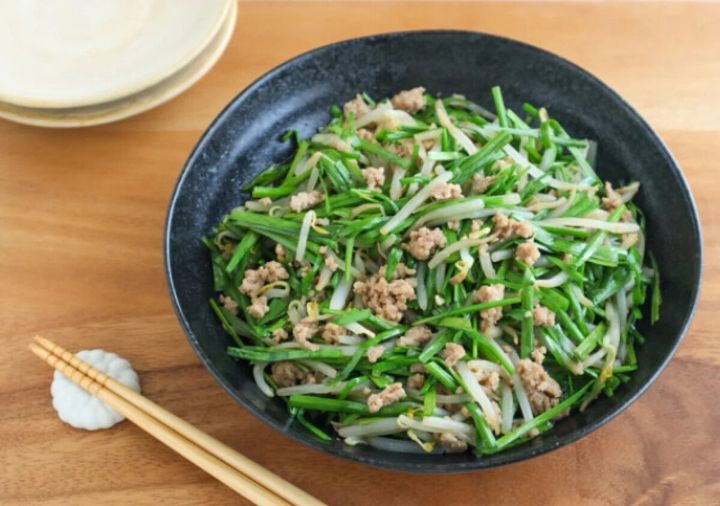 黒い器に盛られたニラ・もやし・豚ひき肉の炒め風。緑のニラがたっぷりで木のテーブルに箸が添えられている