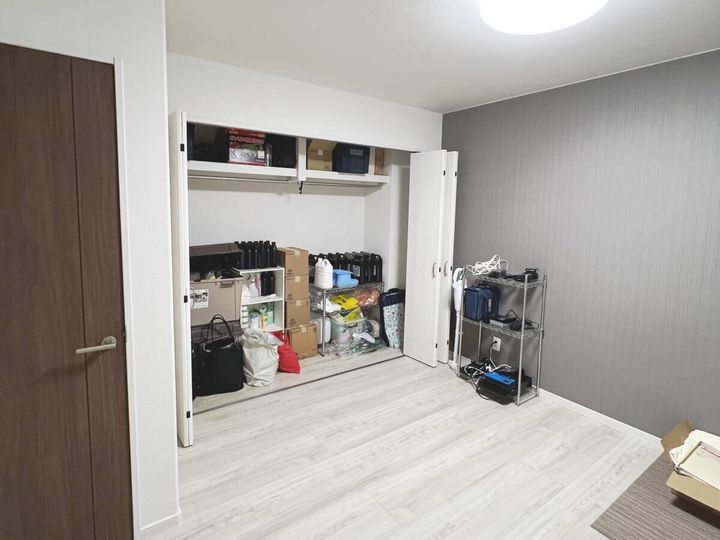 片付け後のすっきりした洋室。開いたクローゼットの中に収納用品やスチールラックが整理して収められ、床にモノがない状態