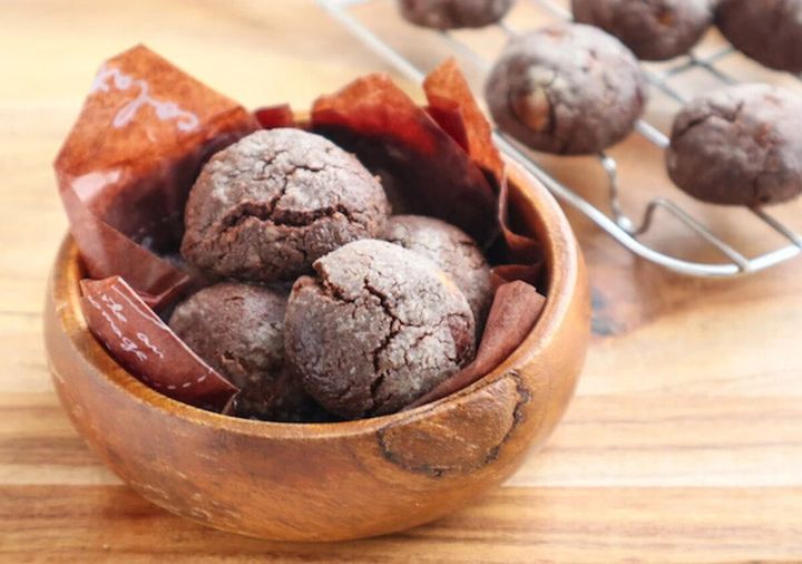 木のボウルに敷いた茶色いワックスペーパーの上に盛られた、表面がひび割れたチョコクラックルクッキー