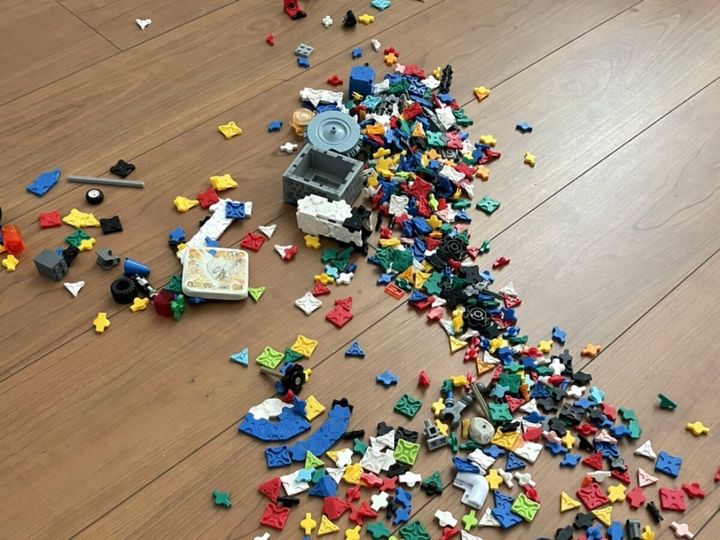 木目のフローリングの床一面に散らばったカラフルな組み立てブロックのおもちゃ