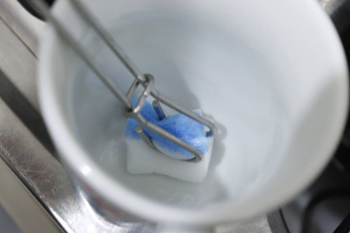 スポンジ用トングで白いマグカップの底をメラミンスポンジで磨く様子