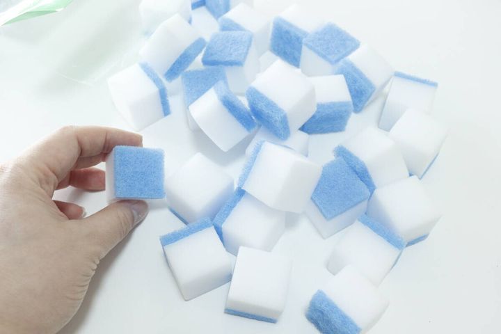 青いポリエステル層が付いた白いメラミンスポンジを手に持つ様子
